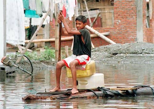 Barn på en improviseret tømmerflåde i en oversvømmet gade i Ecuador under El Niño 1997-98.