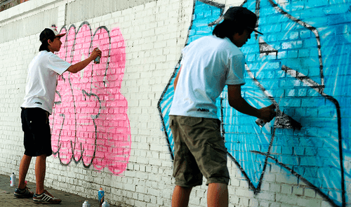 Graffitimalere spraymaler tags på en hvid mur.