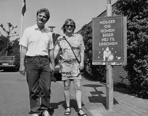 Sort-hvidt fotografi af SF's formand Holger K. Nielsen og hans hustru ved siden af en valgplakat med teksten »Holger og konen siger nej til unionen«. Billedet er fra nej-kampagnen op til folkeafstemningen om Maastricht-traktaten i 1992