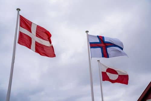 De danske, færøske og grønlandske flag med grå skyer i baggrunden. Billedet er taget i Hoyvik..