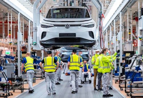 En elbil på samlebånd i en bilfabrik. Flere medarbejdere arbejder omkring bilen i produktionshallen. Billedet illustrerer industrienes behov for kritiske råstoffer til blandt andet elbiler og batterier.