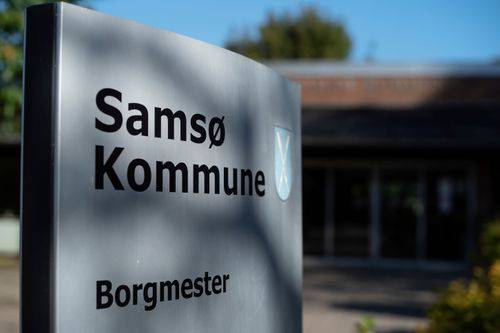 Skilt med teksten "Samsø Kommune". I baggrunden Samsøs rådhus.
