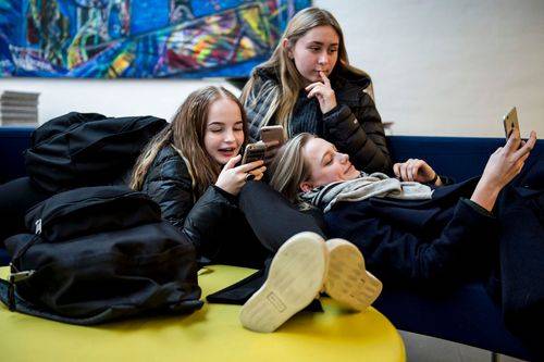 Tre unge piger med mobiltelefoner i en sofa.