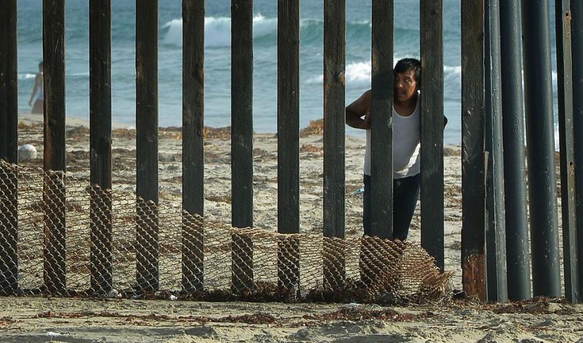 En mexicansk mand kikker mod USA på grænsen mellem USA og Mexico.