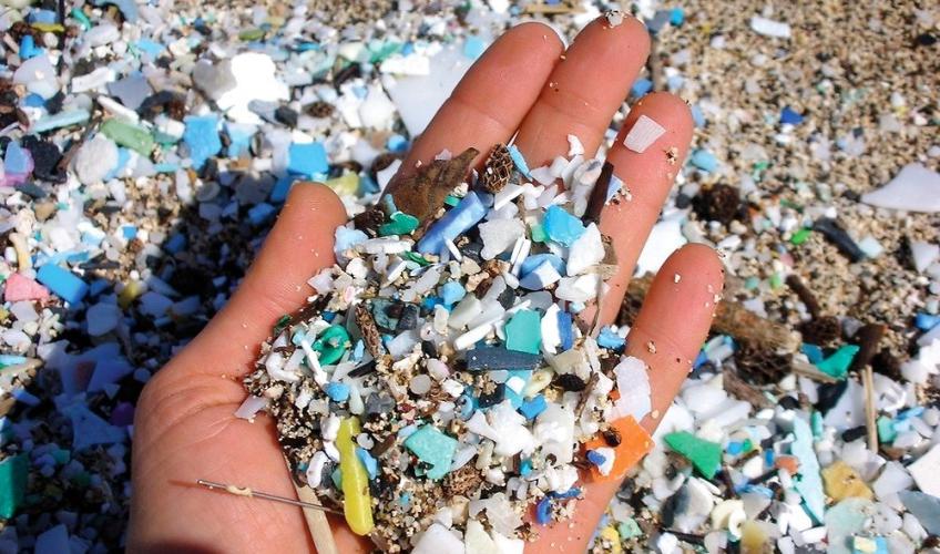 En hånd har samlet en håndfuld sand op, som er fyldt med små plastikstykker