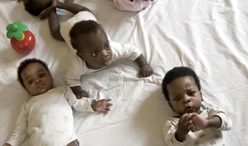 Tre afrikanske babyer ligger på en seng og kigger op