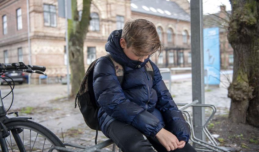 Dreng sidder ked af det og alene foran skole. Det regner og det er vinter.