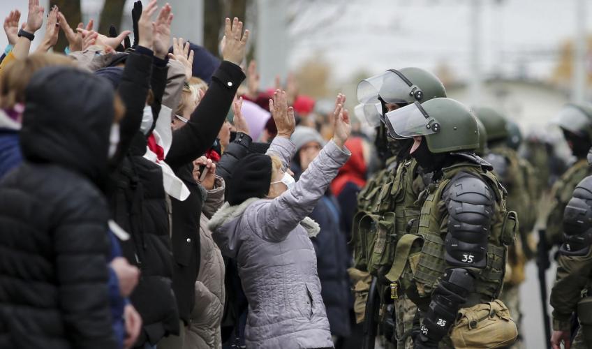 Demonstranter står med hånden i vejret foran politi i kampuniform