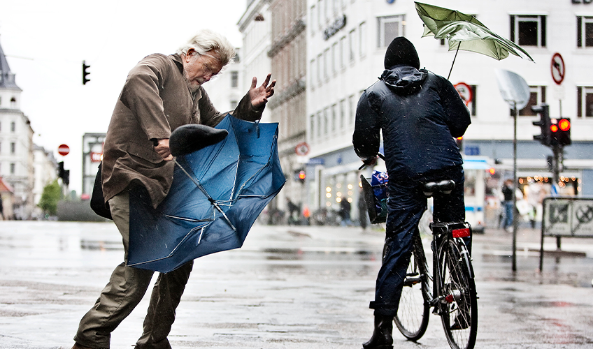 En fodgænger og en cyklist kæmper med hver deres paraply i stormvejr