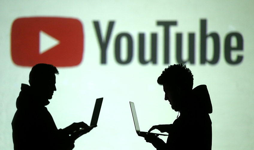 Silhuetter af computerbrugere foran en stor skærm med YouTube-logo.