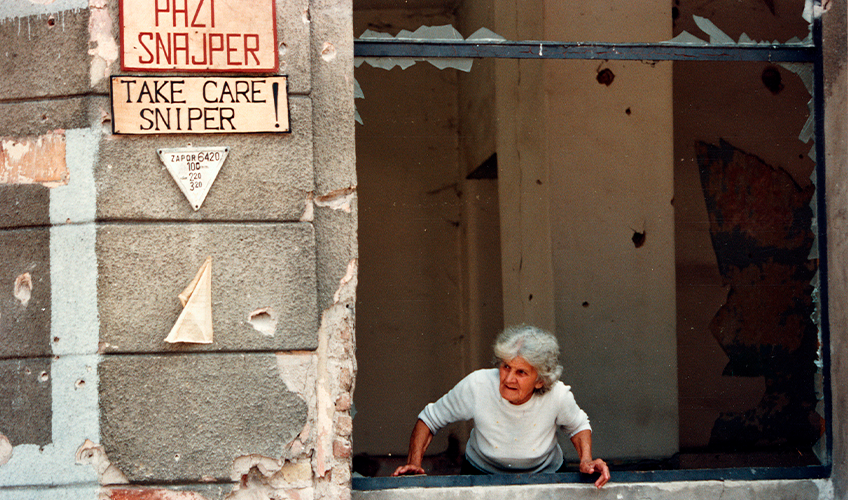 Kvinde i vindue kigger efter flygtende fodgængere i Sarajevo